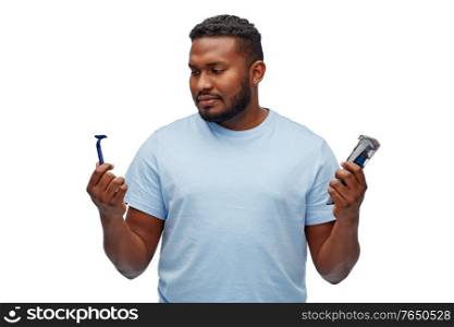shaving, grooming and people concept - young african american man choosing between manual razor blade and trimmer over white background. african man with razor blade and trimmer
