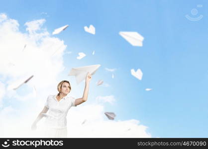 She is acting like child. Young carefree woman with paper plane in hands