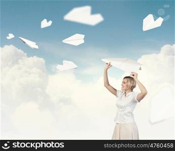 She is acting like child. Young carefree woman with paper plane in hands