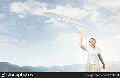 She is acting like child. Young carefree woman with paper plane in hands