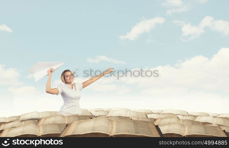 She is acting like child. Young carefree woman with paper plane in hands