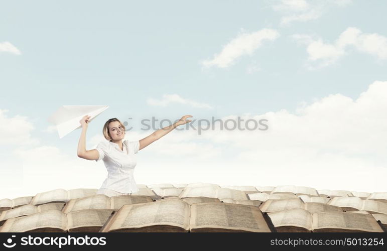 She is acting like child. Young carefree woman with paper plane in hands