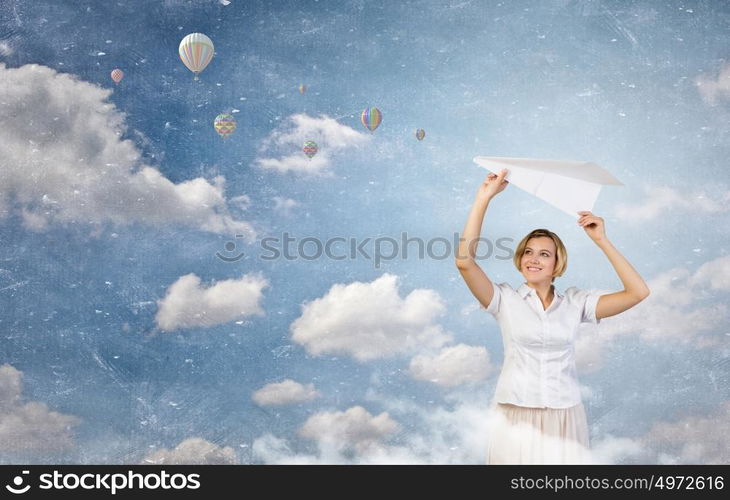 She is adult but still feeling playful . Young cheerful pretty woman playing with paper plane