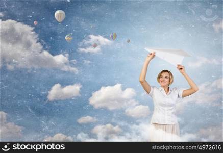 She is adult but still feeling playful . Young cheerful pretty woman playing with paper plane