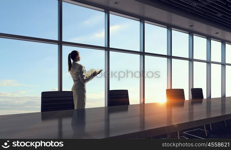 She is an early riser. Mixed media. Businesswoman in night office against panoramic window in light of sunset