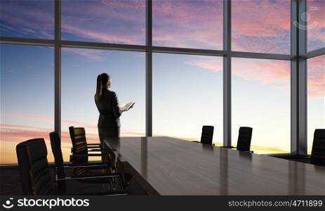 She is an early riser. Mixed media. Businesswoman in night office against panoramic window in light of sunset