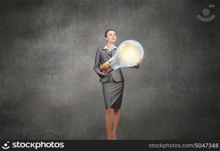 She is carrying her idea. Young businesswoman carrying big light bulb in hands