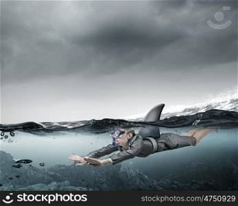 She is dangerous like shark. Young businesswoman with shark flipper swiming under water