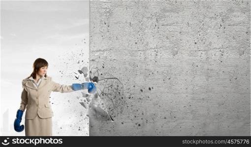 She is fighter. Young businesswoman in blue boxing gloves punching wall