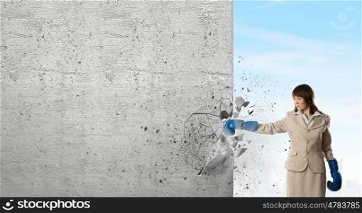 She is fighter. Young businesswoman in blue boxing gloves punching wall