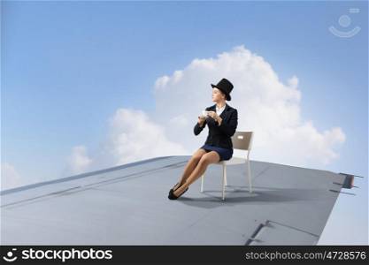 She is flying high. Young businesswoman sitting on edge of airplane wing