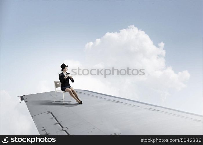 She is flying high. Young businesswoman sitting on edge of airplane wing