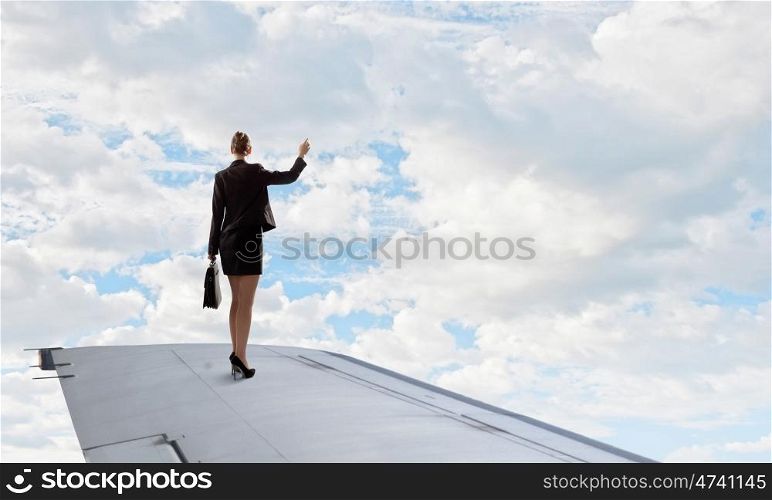 She is flying high. Young businesswoman standing on edge of airplane wing