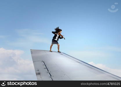 She is flying high. Young businesswoman standing on edge of airplane wing