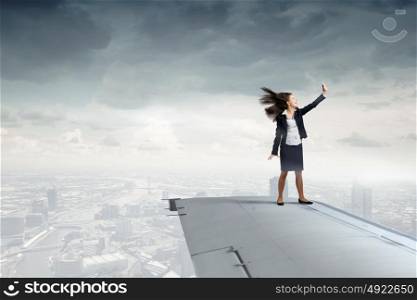 She is flying high. Young businesswoman standing on edge of airplane wing