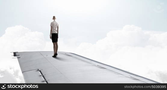 She is flying high. Young businesswoman standing on edge of airplane wing