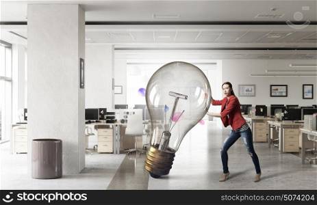 She is got great idea. Elegant businesswoman in modern office interior pushing big bulb