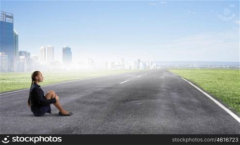 She is in dispair and isolation. Bored young businesswoman sitting alone on asphalt road
