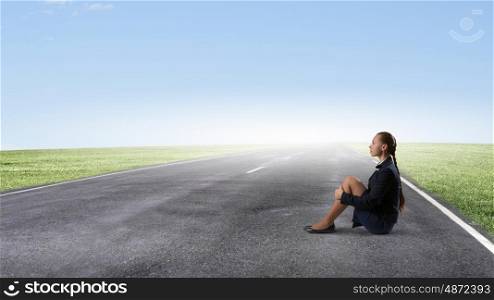 She is in dispair and isolation. Bored young businesswoman sitting alone on asphalt road