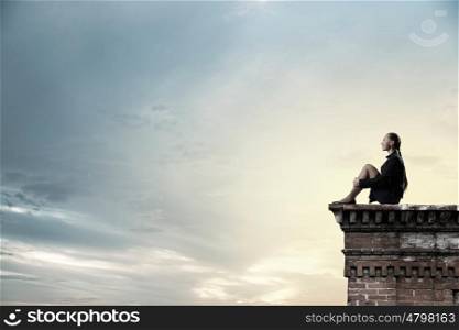 She is in dispair and isolation. Bored young businesswoman sitting alone on building top