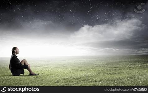 She is in dispair and isolation. Bored young businesswoman sitting alone on green grass
