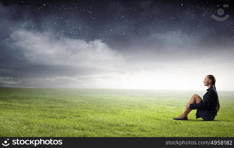 She is in dispair and isolation. Bored young businesswoman sitting alone on green grass