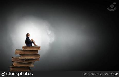 She is in dispair and isolation. Bored young businesswoman sitting alone on pile of books
