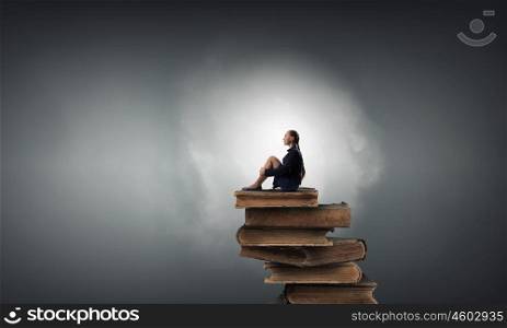 She is in dispair and isolation. Bored young businesswoman sitting alone on pile of books