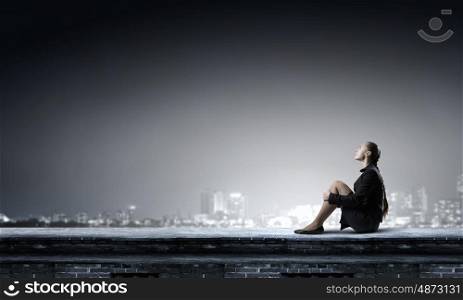 She is in dispair and isolation. Bored young businesswoman sitting alone on roof