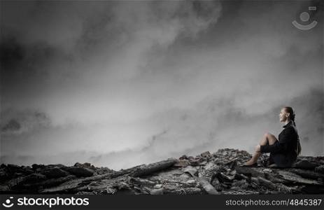 She is in dispair and isolation. Thoughtful young businesswoman sitting alone on rock top
