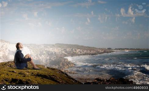 She is in dispair and isolation. Thoughtful young businesswoman sitting alone on rock top