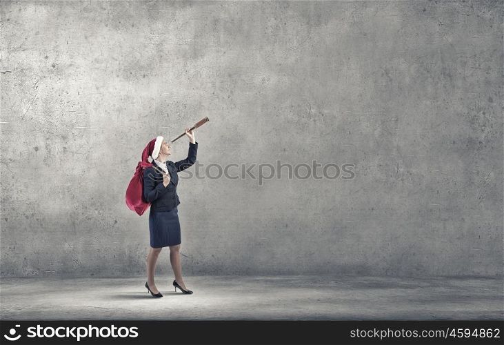 She is looking forward Christmas. Woman in formal suit and Santa hat looking in spyglass