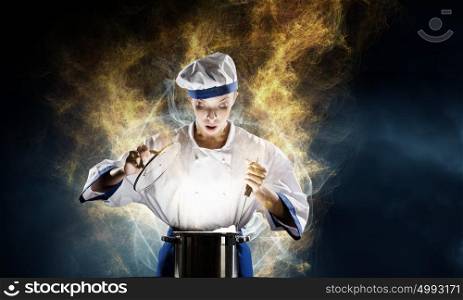She is magician as cook. Pretty woman cook in hat and apron with doing magic above pot