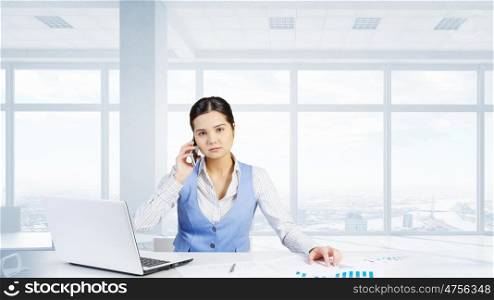 She is making important calls. Young businesswoman at desk in office talking on mobile phone