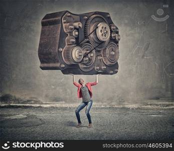 She is not afraid of hard work. Young woman in red jacket lifting big gear mechanism above head