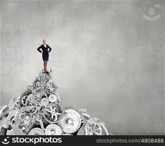 She is on top. Confident businesswoman standing on top of gears
