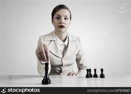 She is playing her game. Young pretty businesswoman sitting at table and playing chess