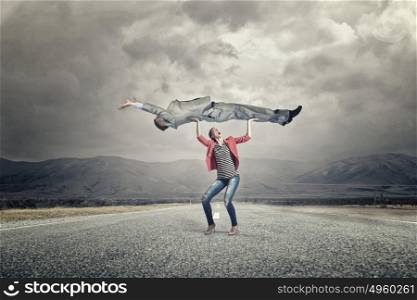 She is powerful and determined. Young woman in red jacket lifting man above head