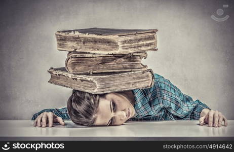 She is preparing for exams. Student girl pressed with pile of books to table