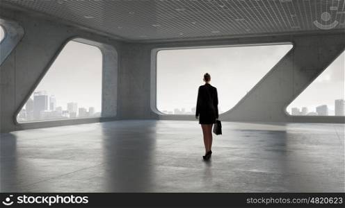 She is ready to face new day. Businesswoman with suitcase in modern interior looking in office window
