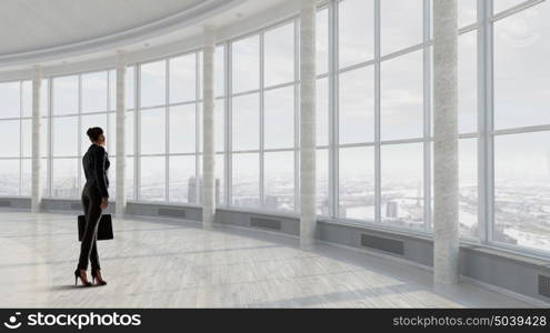 She is ready to face new day. Businesswoman with suitcase in modern interior looking in office window