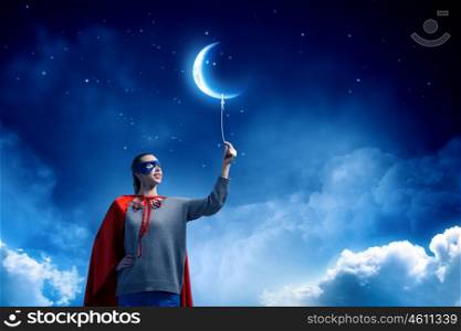 She is super woman. Young confident woman in red cape and mask with moon balloon