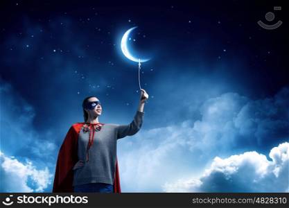 She is super woman. Young confident woman in red cape and mask with moon balloon