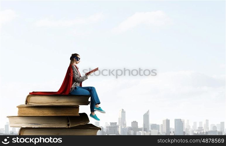 She is super woman. Young thoughtful woman in red cape and mask on building roof read book
