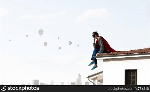 She is super woman. Young thoughtful woman in red cape and mask on building roof