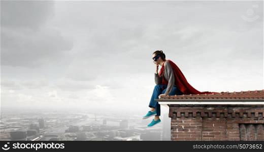 She is super woman. Young thoughtful woman in red cape and mask on building roof
