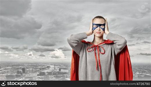 She is super woman. Young woman in red cape and mask covering ears with palms