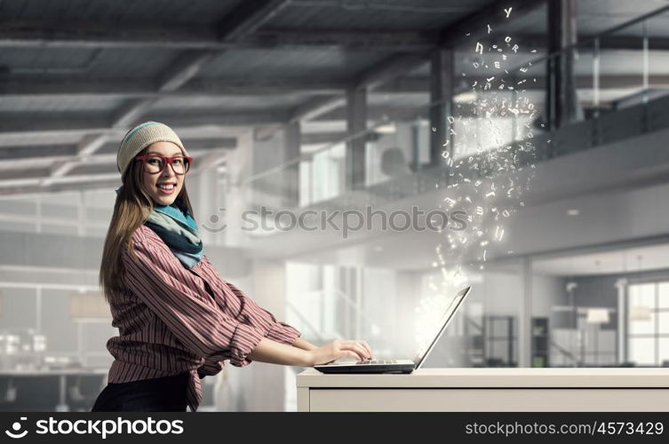 She is surfing the Internet. Young hipster girl sitting at table and working on laptop