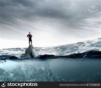 She is top manager. Confident businesswoman with arms on waist standing on rock top in water