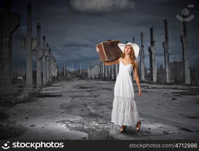 She is traveling light. Woman with suitcase in white long dress and hat